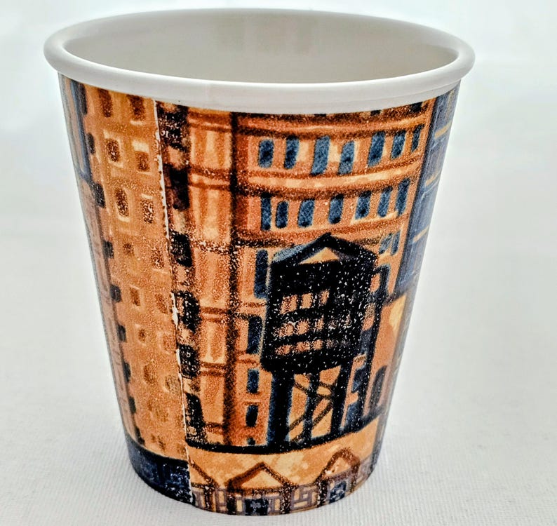 Puede incluir: Una taza de caf&eacute; de papel desechable con un borde blanco y un dise&ntilde;o arquitect&oacute;nico marr&oacute;n y azul. La taza presenta un patr&oacute;n repetitivo de edificios y estructuras.