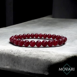May include: A red gemstone bracelet made of round beads. The bracelet is on a gray surface.