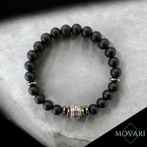 May include: Black matte beaded bracelet with a silver and gold charm featuring Tibetan script.
