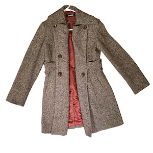 May include: A brown and tan tweed coat with a double-breasted front, featuring four visible dark brown buttons, a wide collar, and long sleeves. The interior is lined with a solid reddish-pink fabric, and a black label with the text GUESS is visible.