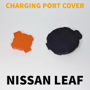 Puede incluir: Dos tapas de puerto de carga para un Nissan Leaf. Una es naranja y la otra es negra.