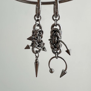 Può includere: Un paio di orecchini d'argento con intricati disegni a catena e accenti appuntiti. Gli orecchini sono sospesi da un cerchio d'argento.