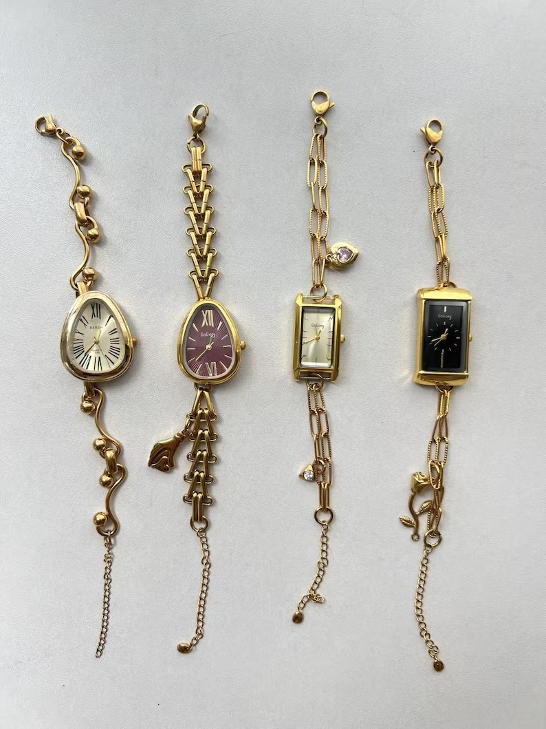 Pode incluir: Quatro rel&oacute;gios dourados com designs &uacute;nicos. Os rel&oacute;gios t&ecirc;m diferentes formatos de mostrador: oval, em forma de gota e retangular. Cada rel&oacute;gio tem um design de pulseira diferente, incluindo corrente e elementos decorativos. Os mostradores s&atilde;o creme, bord&ocirc;, creme e preto.