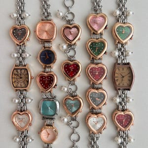 Peut inclure: Un ensemble de dix montres-bracelets argentées et dorées avec des breloques en forme de cœur et des accents de perles. Les montres ont des cadrans de différentes couleurs, notamment rose, vert, rouge, bleu et blanc.