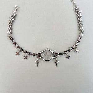 Op de afbeelding: Een zilveren horloge met een witte wijzerplaat en een kettingarmband met stervormige bedels.