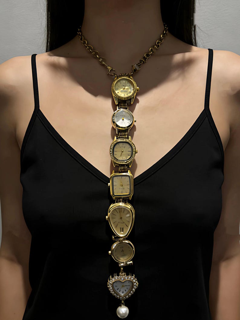 K&ouml;nnte beinhalten: Eine goldfarbene Halskette mit mehreren Vintage-Uhren in verschiedenen Formen und Gr&ouml;&szlig;en. Die Uhren sind vertikal angeordnet, mit einem herzf&ouml;rmigen Anh&auml;nger und einer herabh&auml;ngenden Perle. Die Halskette hat einen Kettenverschluss.