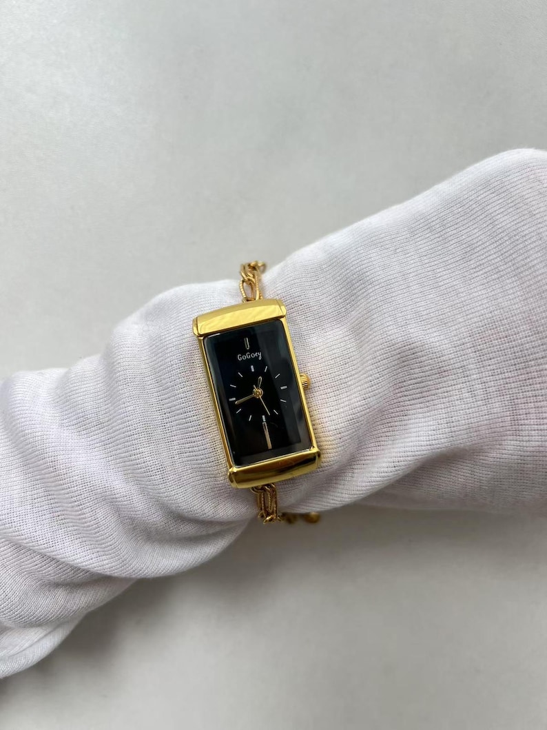 Pode incluir: Rel&oacute;gio retangular dourado com mostrador preto e ponteiros dourados. O rel&oacute;gio tem o nome da marca "GoGoey" impresso no mostrador. O rel&oacute;gio &eacute; preso a uma pulseira de corrente dourada.