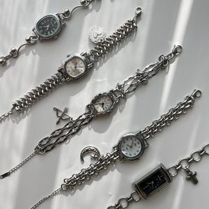 Op de afbeelding: Een verzameling zilverkleurige polshorloges met verschillende kettingontwerpen. Elk horloge heeft een andere wijzerplaatvorm en -stijl, waaronder ovaal, rechthoekig en rond. Sommige horloges hebben decoratieve bedels.