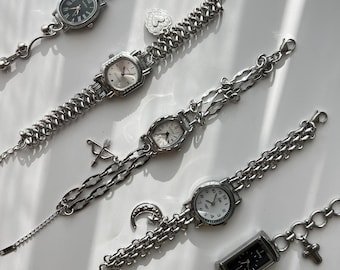 May include: A collection of silver-toned wristwatches with various chain designs. Each watch features a different face shape and style, including oval, rectangular, and round. Some watches have decorative charms like a heart, crescent moon, and cross.