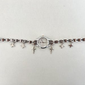 Op de afbeelding: Een zilveren horloge met een witte wijzerplaat en een zilveren kettingarmband met stervormige bedels.