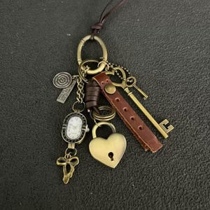 May include: A brown leather cord necklace with a variety of charms, including a small clock, a heart-shaped padlock, a key, and a small metal tag with text.