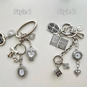 May include: Two silver keychains with different charms. Style 1 features a silver heart charm with the text "Faith, Hope, Love" and a silver watch charm. Style 2 features a silver cross charm, a silver book charm, and a silver watch charm.