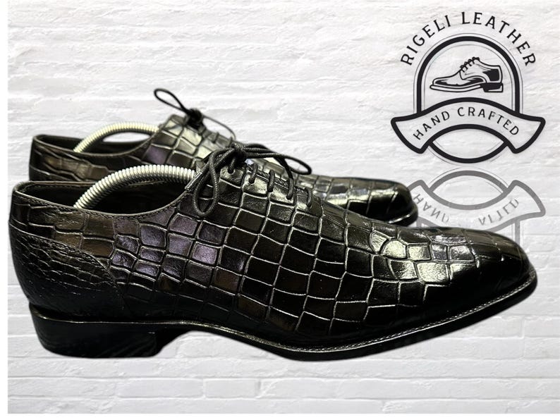 May include: Black leather dress shoes with a crocodile pattern. The shoes have a lace-up closure and a pointed toe. The shoes are made by Rigelli Leather and are hand-crafted.