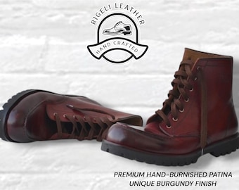 Könnte beinhalten: Ein Paar bordeauxrote Lederstiefel mit braunen Schnürsenkeln und dicken schwarzen Profilsohlen. Die Stiefel haben ein handpoliertes Patina-Finish. Über den Stiefeln steht das Logo RIGELI LEATHER HAND CRAFTED. Darunter: PREMIUM HAND-BURNISHED PATINA UNIQUE BURGUNDY FINISH.