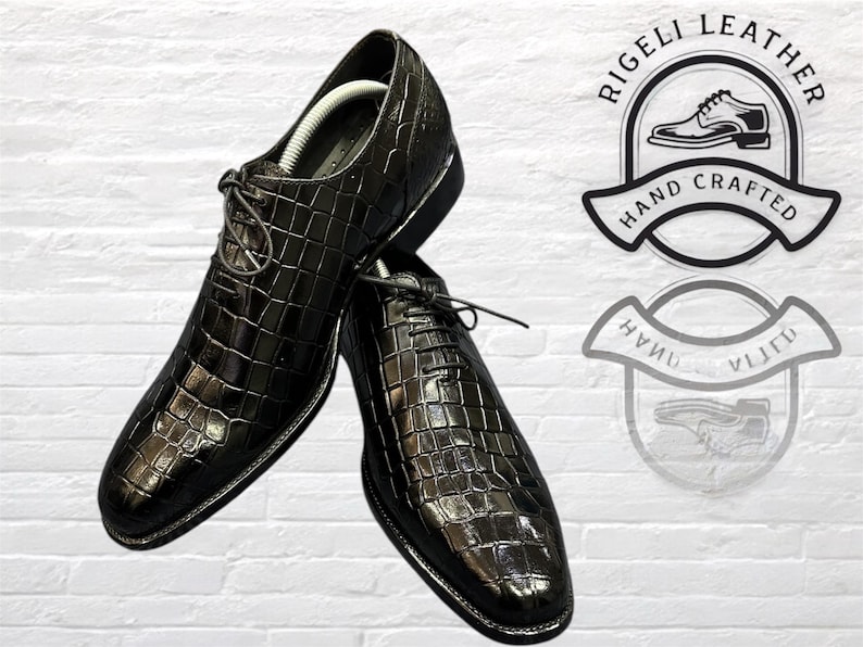 May include: A pair of black leather dress shoes with a crocodile pattern. The shoes have lace-up closures and are made by Rigelli Leather, a company that specializes in hand-crafted footwear.