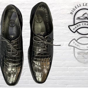 May include: A pair of black leather lace-up shoes with a crocodile-embossed pattern. The shoes have a pointed toe and a low heel. The brand name "Rigelli Leather" is printed on the shoes.