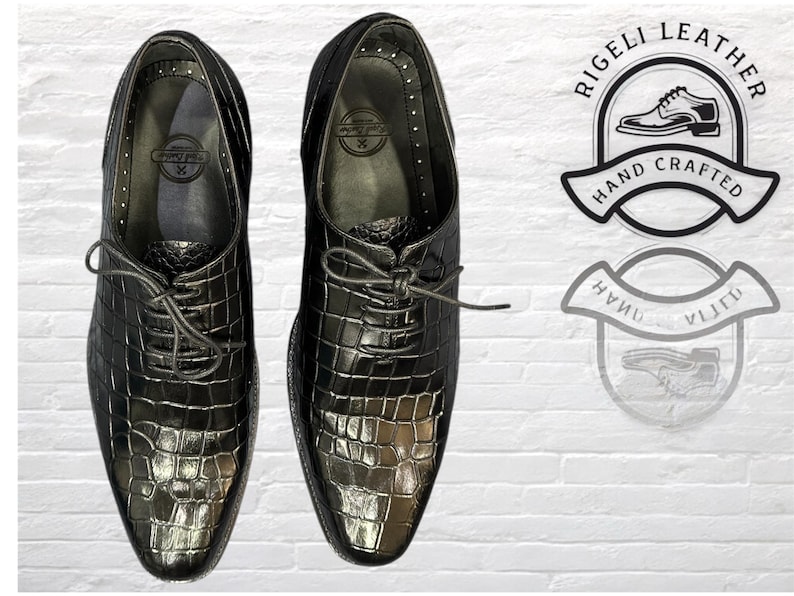 May include: A pair of black leather lace-up shoes with a crocodile-embossed pattern. The shoes have a pointed toe and a low heel. The brand name "Rigelli Leather" is printed on the shoes.