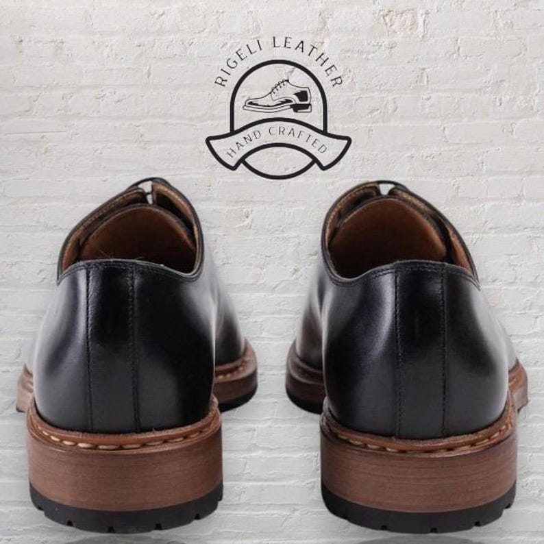 May include: A pair of black leather oxford shoes with brown soles. The shoes are hand-crafted and feature the text "Rigelli Leather Hand Crafted".