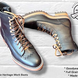 Puede incluir: Botas de trabajo de cuero negro con cordones marrones, un detalle de flecos tipo kiltie sobre la puntera, construcción con vira Goodyear y una suela gruesa con tacos. Las botas llevan la etiqueta Rigeli Leather Hand Crafted.