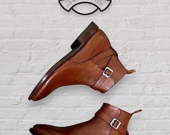 Könnte beinhalten: Ein Paar braune Lederstiefel mit Schnallenriemen. Die Stiefel haben eine spitze Zehenpartie und einen niedrigen Absatz. Die Stiefel sind aus hochwertigem Leder gefertigt und handgefertigt.