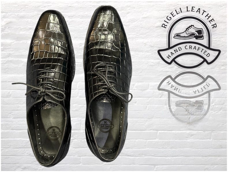May include: A pair of black leather dress shoes with crocodile embossed pattern. The shoes have lace-up closures and are hand-crafted.