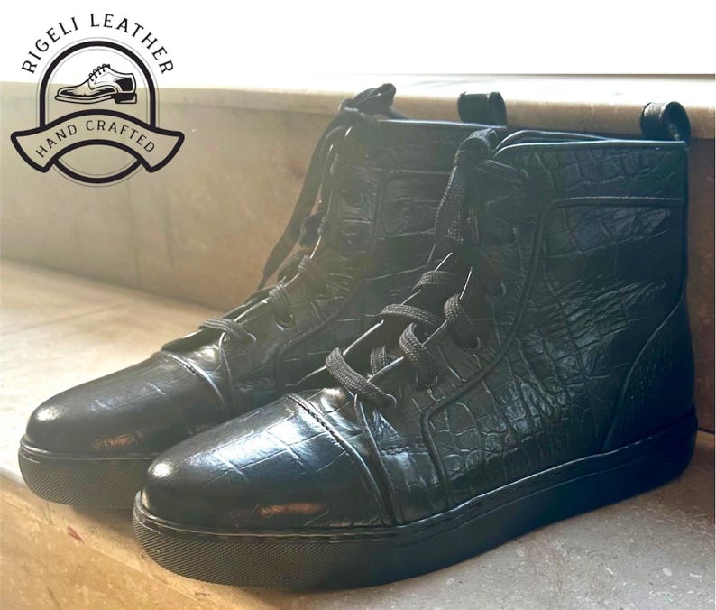 May include: Pair of black leather high-top sneakers with a textured, crocodile-like pattern. The sneakers have black laces and soles. The image includes a logo that says "Rigeli Leather" and "Hand Crafted".