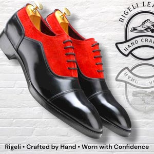 May include: Pair of black leather dress shoes with red suede panels. The shoes have a glossy finish and are laced up with black laces. The image includes the text "Rigeli &bull; Crafted by Hand &bull; Worn with Confidence."