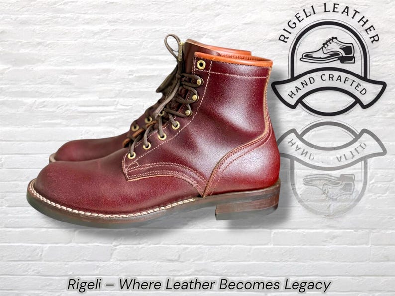 Puede incluir: Botas de cuero burdeos con dise&ntilde;o de cordones y ojales dorados. Las botas tienen una suela resistente y un cuello marr&oacute;n en contraste. El texto "Rigeli - Where Leather Becomes Legacy" est&aacute; en la parte inferior.