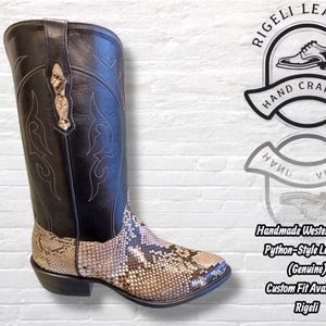 Pu&ograve; includere: Stivale western fatto a mano in pelle nera e marrone stile pitone. Lo stivale ha una tomaia nera con cuciture decorative e un motivo a pelle di serpente nella parte inferiore. Il testo "Rigeli Leather" e "Hand Crafted" &egrave; visibile.