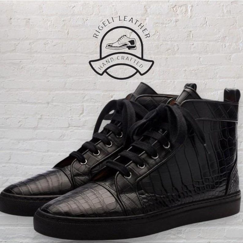May include: Black high-top sneakers with a textured, crocodile-like pattern. The sneakers have black laces and soles. The image includes a logo that says "Rigeli Leather Hand Crafted".