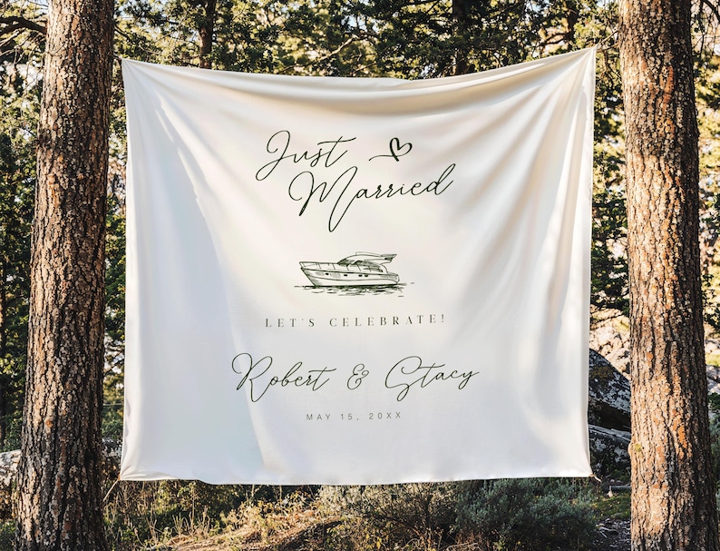May include: A white fabric banner with the words "Just Married" and a heart symbol in elegant script. Below is a drawing of a boat, followed by "LET'S CELEBRATE!" and the names "Robert & Stacy" with a date. The banner is hanging between two trees.