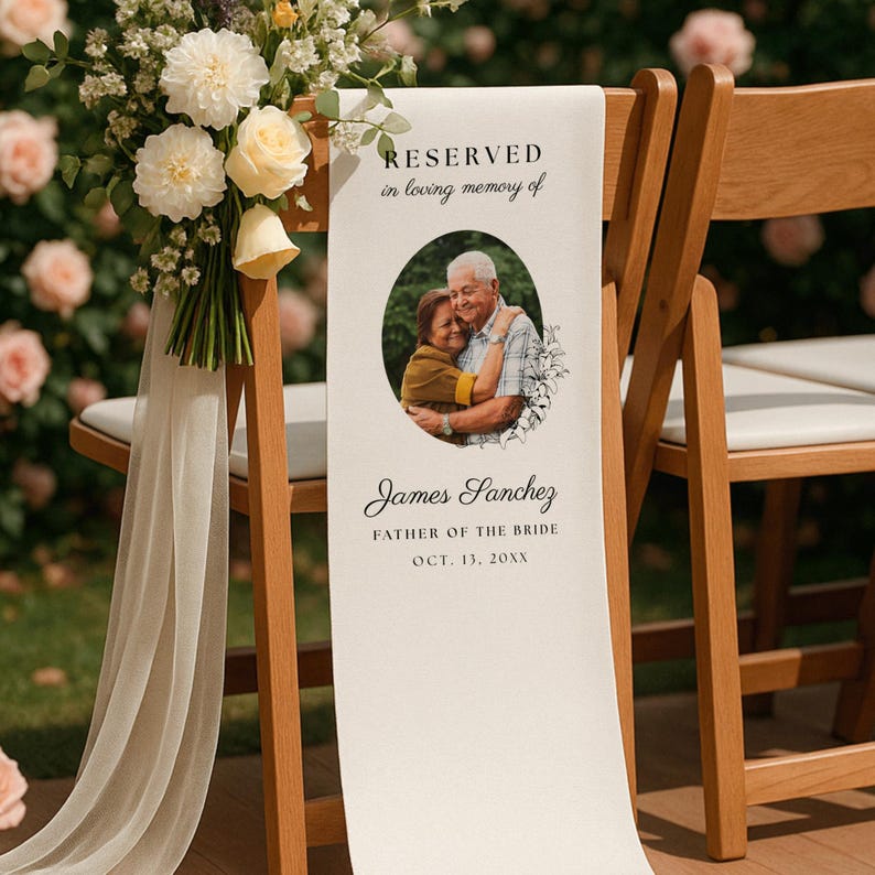 May include: A white fabric memorial sign draped over a wooden chair, featuring the text RESERVED in loving memory of, a circular photograph of two people, and the name James Sanchez, FATHER OF THE BRIDE, OCT. 13, 20XX, with a floral bouquet.