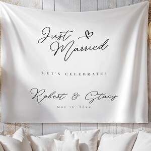 May include: White fabric backdrop with the words "Just Married" in elegant black script, along with "Let's Celebrate!" and the names "Robert & Stacy" with a date. Gold and white balloons are visible.