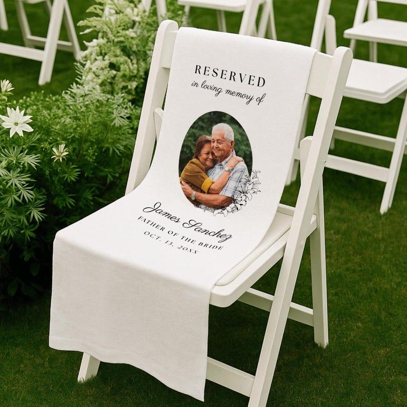 May include: A white fabric memorial sign draped over a white folding chair. The sign features the text RESERVED in loving memory of, a circular photograph of two people embracing, and the name James Sanchez, FATHER OF THE BRIDE, OCT. 13, 20XX.