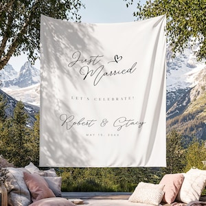 Peut inclure: Bannière en tissu blanc avec les mots "Just Married" en écriture élégante, un symbole de cœur et les noms Robert & Stacy avec la date du 15 mai 20XX. La bannière est suspendue à l'extérieur avec un arrière-plan de montagne.