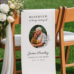 May include: A white fabric memorial sign draped over a wooden chair, featuring the text RESERVED in loving memory of, a circular photo of two people embracing, and the name James Sanchez, FATHER OF THE BRIDE, OCT. 13, 20XX with floral accents.