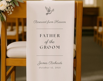 May include: A white fabric sign draped over a wooden chair, featuring a black dove illustration and the text: Reserved from Heaven, FATHER of the GROOM, James Richards, October 12, 2021. The sign is decorated with white flowers at the top left corner.
