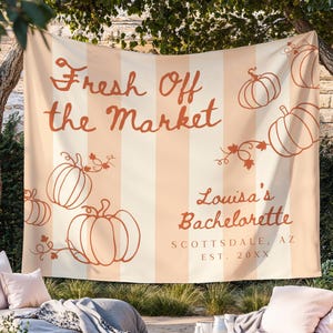 Może przedstawiać: Brzoskwiniowo-kremowy sztandar w paski z napisem "Fresh Off the Market" i "Louisa's Bachelorette" w ozdobnej czcionce. Obrysowane dynie i winorośle zdobią sztandar. Lokalizacja to Scottsdale, AZ, z datą założenia.