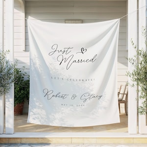 May include: White fabric banner with the words "Just Married" and a heart symbol in elegant black script. Below, it reads "Let's Celebrate!" and the names "Robert & Stacy" with a date. Wedding decor.
