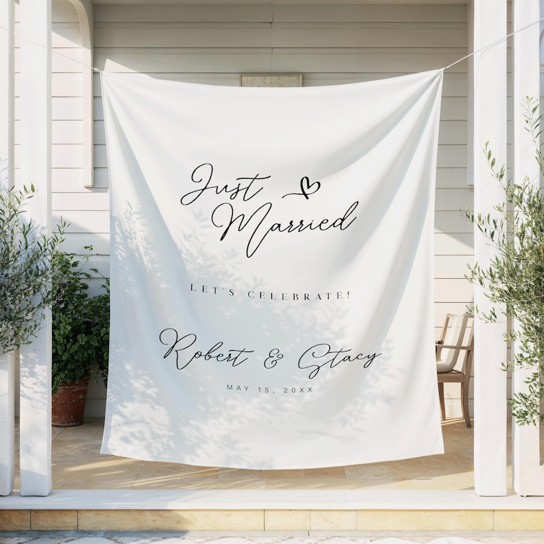 May include: White fabric banner with the words "Just Married" and a heart symbol in elegant black script. Below, it reads "Let's Celebrate!" and the names "Robert & Stacy" with a date. Wedding decor.