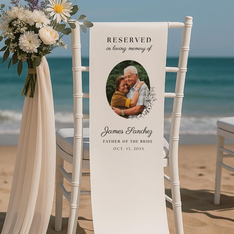 May include: A white wedding chair featuring a vertical memorial sign with a photo of two people in an oval frame. The text reads RESERVED in loving memory of James Sanchez FATHER OF THE BRIDE OCT. 13, 20XX. A bouquet of white flowers is attached.