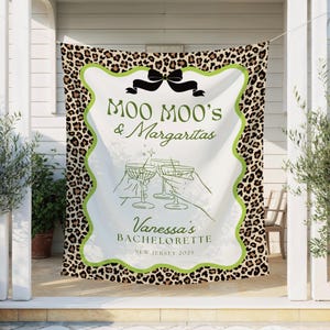 May include: A white banner with a leopard print border and a green wavy outline. The banner reads "Moo Moo's & Margaritas" with a bow above and "Vanessa's Bachelorette New Jersey 2025" below, with illustrations of hands toasting.