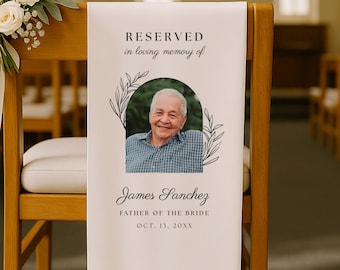 May include: A white fabric memorial sign draped over a wooden chair, featuring the text RESERVED in loving memory of, a photo of an older man, and the name James Sanchez, FATHER OF THE BRIDE, OCT. 13, 20XX, framed by black line-art botanical leaves.