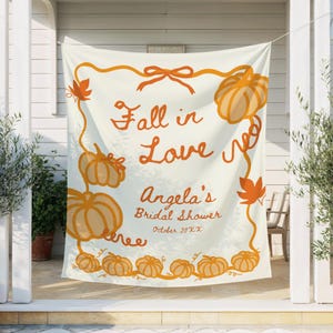 May include: A cream-colored banner with orange pumpkins and fall leaves. The text "Fall in Love" is written in cursive, with "Angela's Bridal Shower" and the date below. The banner is hanging outside.