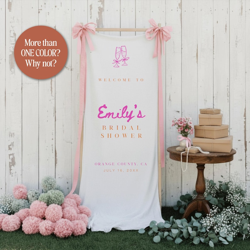 Puede incluir: Un cartel de bienvenida de despedida de soltera de tela blanca con texto y acentos rosas. El letrero dice "Emily's Bridal Shower" e incluye la fecha y el lugar. Arcos y cintas rosas adornan la parte superior. Una peque&ntilde;a mesa contiene regalos y flores.