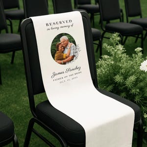 May include: A white memorial chair sign draped over a black chair. The sign features the text RESERVED in loving memory of, a circular photograph of two people embracing, and the name James Sanchez, FATHER OF THE BRIDE, and OCT. 13, 20XX.