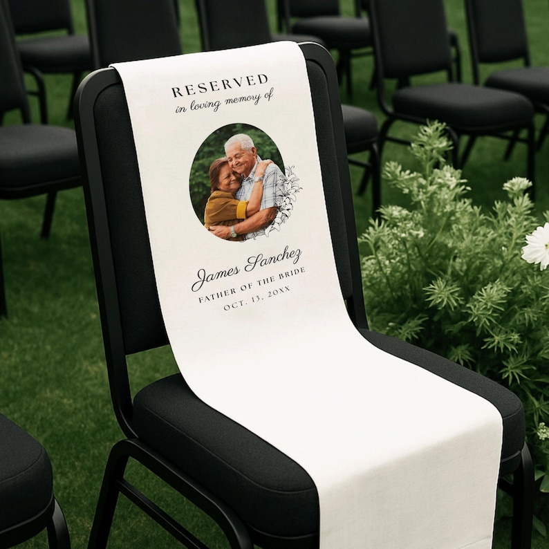 May include: A white memorial chair sign draped over a black chair. The sign features the text RESERVED in loving memory of, a circular photograph of two people embracing, and the name James Sanchez, FATHER OF THE BRIDE, and OCT. 13, 20XX.