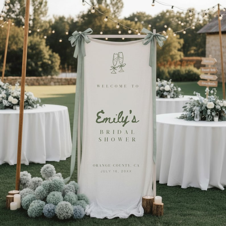 Puede incluir: Un cartel de bienvenida a una despedida de soltera blanco con texto verde que dice "Bienvenida a la despedida de soltera de Emily". El cartel est&aacute; decorado con cintas verdes y copas de champ&aacute;n. El evento es en Orange County, CA, el 16 de julio de 20XX.