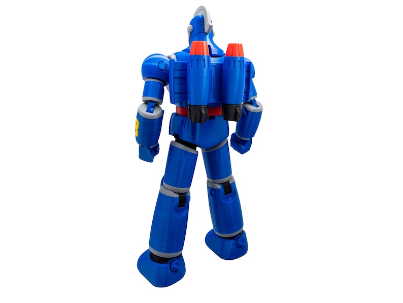 May include: A blue robot action figure with a silver head and red and orange jetpacks. The figure has articulated joints and gray accents. The robot is standing on a white surface.