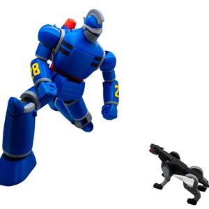 May include: A blue robot action figure with yellow number details and a silver helmet is posed in a dynamic stance. A smaller black and gray robotic dog figure is positioned nearby. The figures are set against a white background.